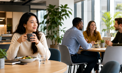 Pessoa aproveita o horário de almoço no trabalho em momento tranquilo enquanto colegas conversam ao fundo.